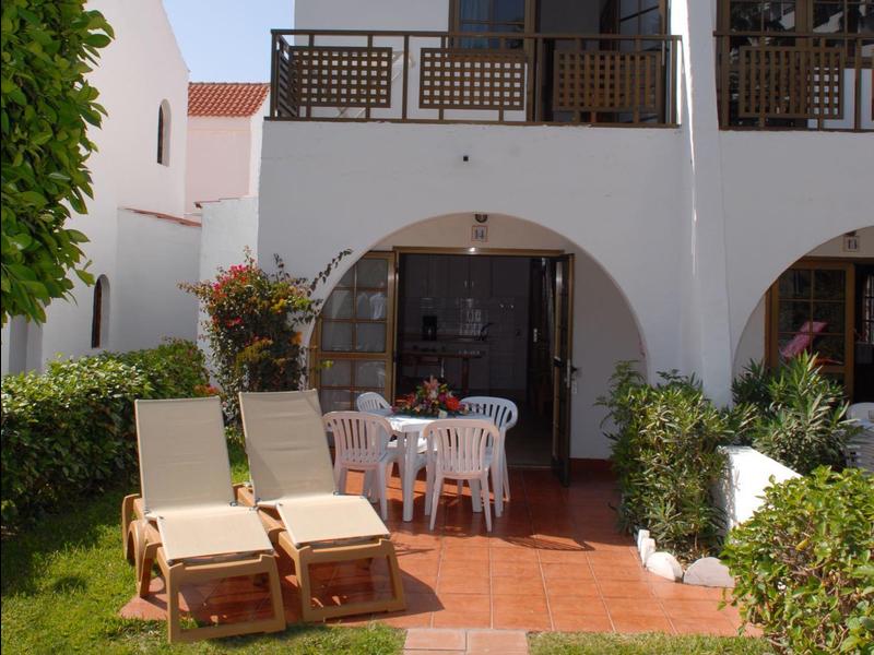 Twee verdiepingen tellend wit vakantiehuis met terrasmeubilair en ligstoelen in de tuin.