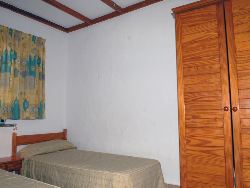 Eenvoudige hotelkamer met eenpersoonsbed, kleurrijk gordijn en kleine houten kast.