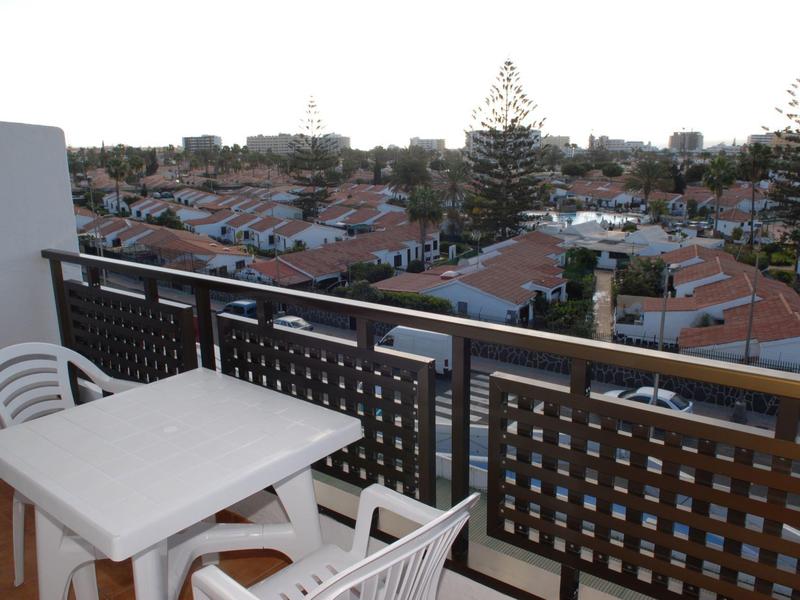 Balkon met tafel en stoelen met uitzicht op rijen huizen en bomen onder bewolkte lucht.