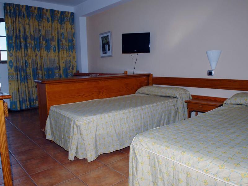 Hotelkamer met twee eenpersoonsbedden, aan de muur gemonteerde tv en geel-blauwe patroon gordijnen