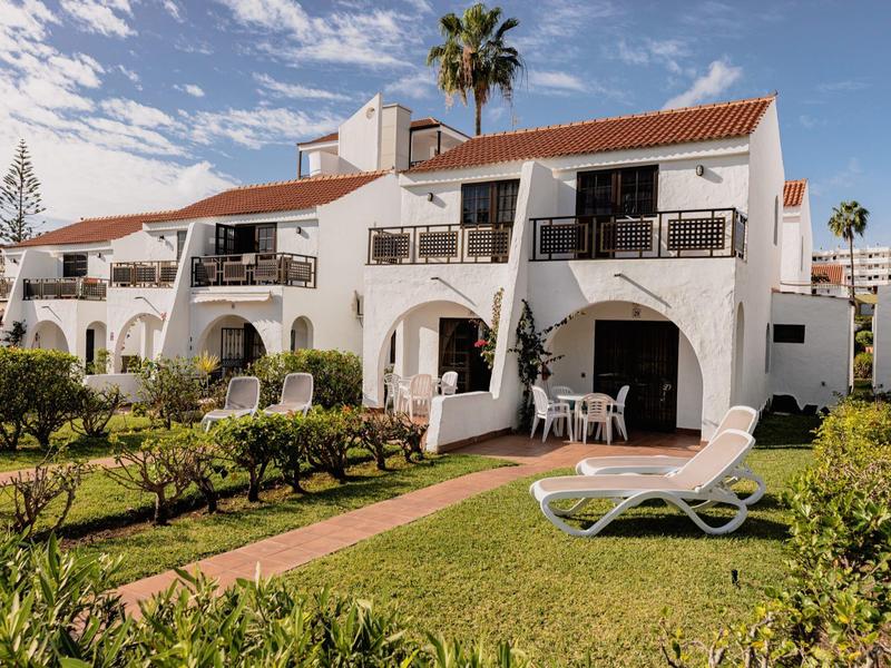 Wit hotelgebouw met rode daken en balkons, omgeven door groene tuinen en ligstoelen.