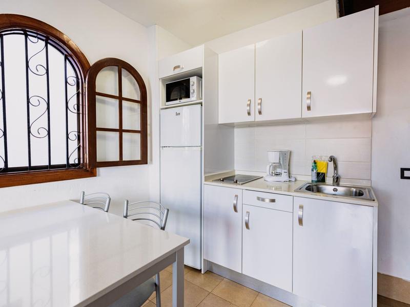 Kleine keuken met witte kasten, magnetron, koelkast en gootsteen naast een groot raam.