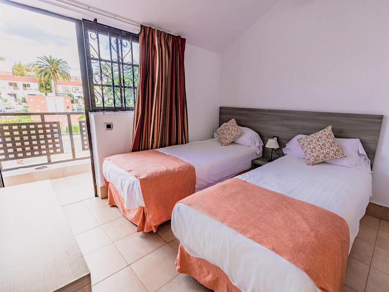 Tweepersoonskamer met witte lakens en oranje dekens, balkon met uitzicht op palmbomen
