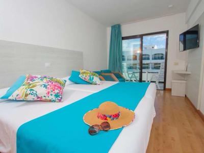 Bright hotel room with two beds, colorful pillows, and balcony with glass front.