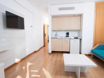 Modern living space with kitchenette, sofa, TV, and wooden floor in bright interior.