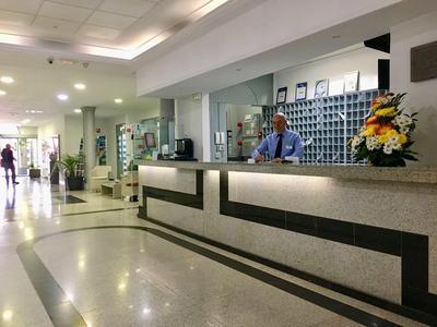 Hotel reception with staff member behind the counter and floral arrangement.