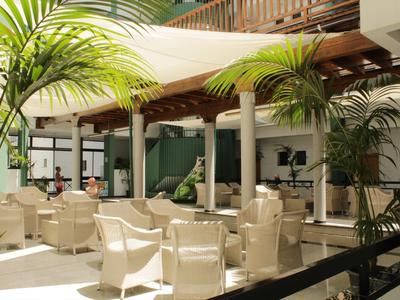Bright hotel lounge with white chairs, wooden elements, and tropical plants.