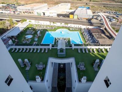 Blick von oben auf einen Hotelpool mit Liegestühlen und grünen Rasenflächen.
