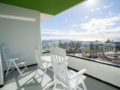 Balkon mit weißen Stühlen und Blick auf Meer und Stadt am Tag.