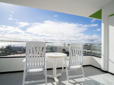 Zwei weiße Stühle und ein runder Tisch auf einem Balkon mit Aussicht auf die Stadt und Himmel.