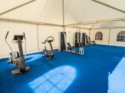 Fitnessbereich in einem Zelt mit stationären Trainingsgeräten und blauem Teppichboden.