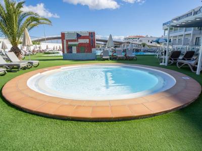 Runder Pool mit Liegestühlen und Sonnenschirmen an einem sonnigen Tag in Hotelanlage.
