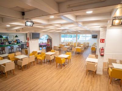 Weißer Hotel-Speisesaal mit Holzboden, gelben Stühlen und rechteckigen Tischen in Reihen.