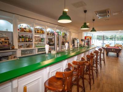 Moderner Hotelbarbereich mit grünem Tresen und Holzstühlen, helle Atmosphäre.