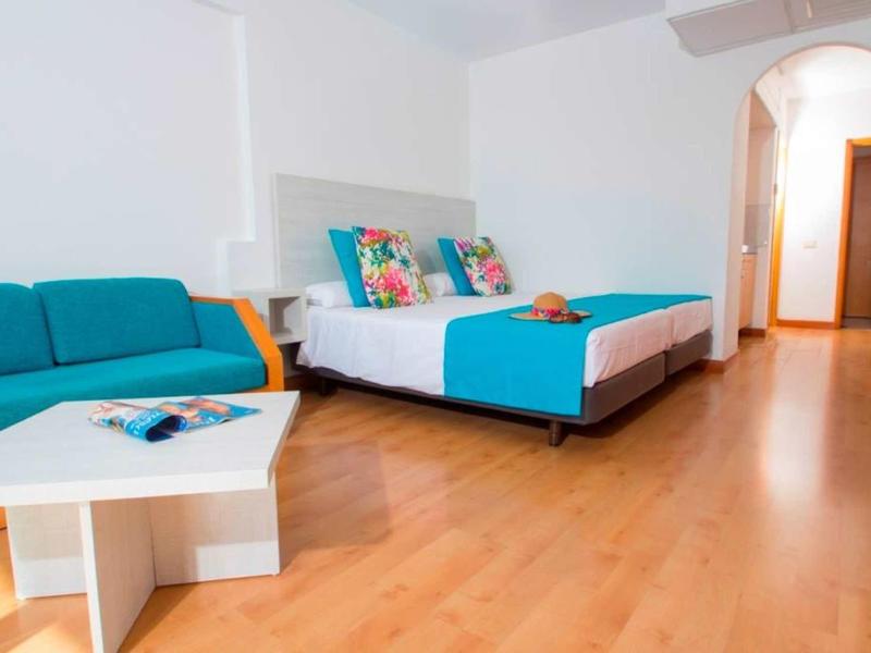 Bedroom with double bed, blue sofa, and light wooden floor in a hotel room.