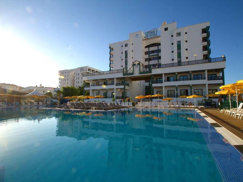 Large hotel with outdoor pool and sun loungers on a sunny day.