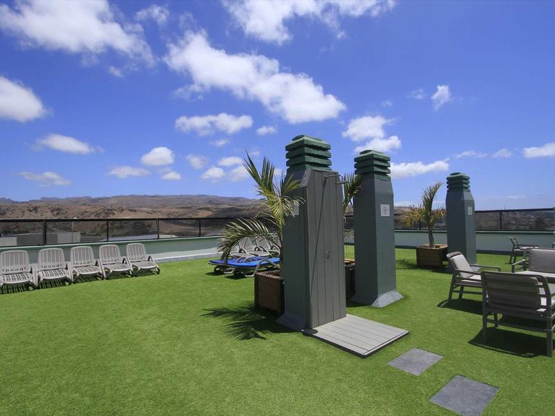 Rooftop terrace with lounge chairs, seating area, and umbrellas under a blue sky.