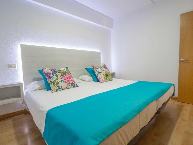 Modern hotel room with two beds, turquoise bedspread, and floral pillows.