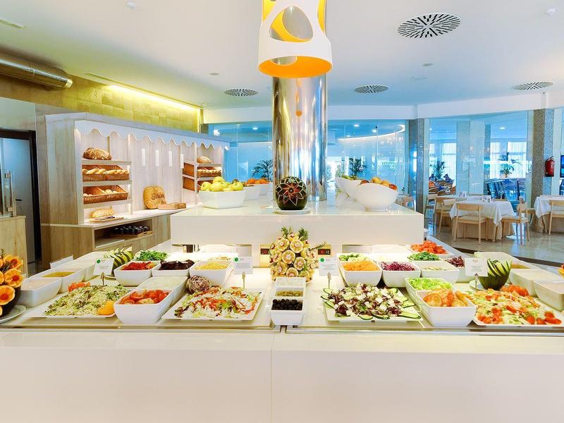 Buffet mit vielfältigen Salaten, frischem Obst und dekorativen Blumen in hellem Restaurant.