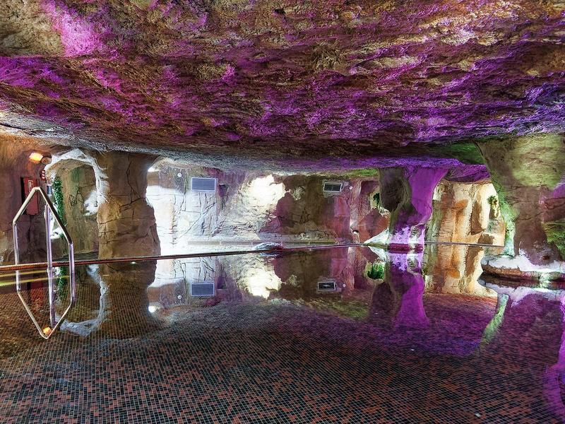 Unterirdischer Raum mit stillstehendem Wasser, beleuchtet von violettem und gelbem Licht.