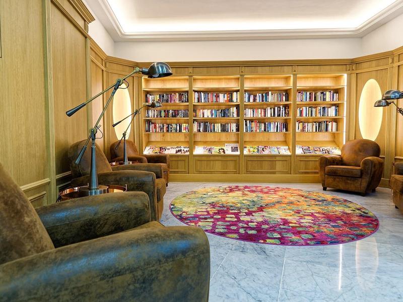 Gemütlicher Lesezimmer mit Ledersesseln, Bücherregal aus Holz und teppich mit buntem Muster.