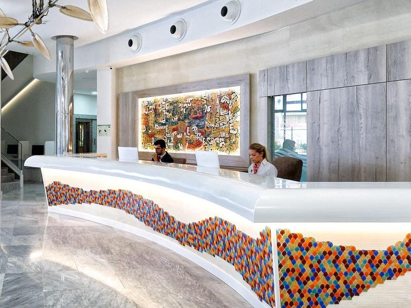 Moderner Empfang mit geschwungenem weißen Tresen, buntem Mosaikmuster und grauer Wandgestaltung.