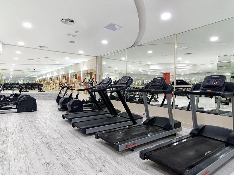 Moderner Fitnessraum mit mehreren Laufbändern, Steppern und hellen Holzböden, großflächige Spiegelwand.