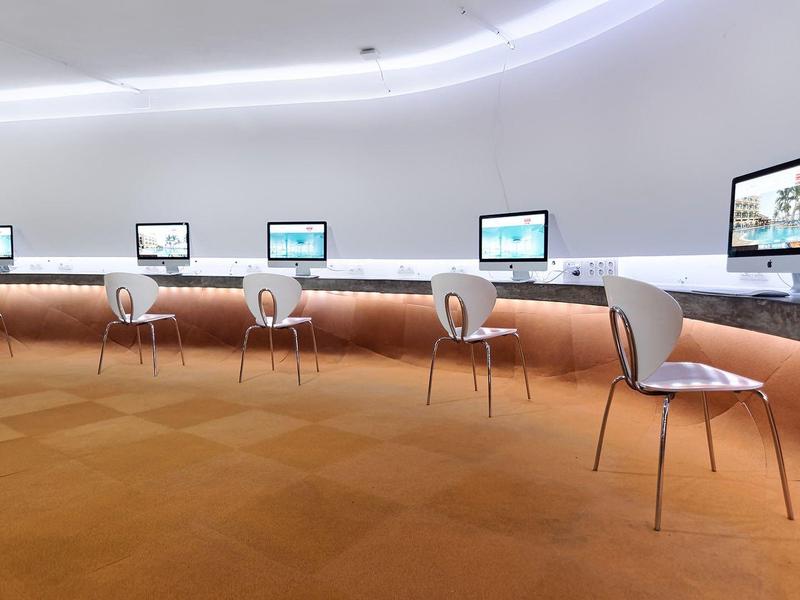 Moderner Computerraum mit weißen Stühlen und mehreren Bildschirmen an einer gebogenen Wand.