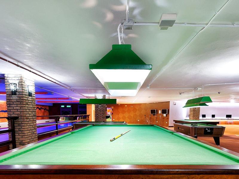 Innenraum einer Billardhalle mit mehreren Billardtischen und kräftiger Beleuchtung.