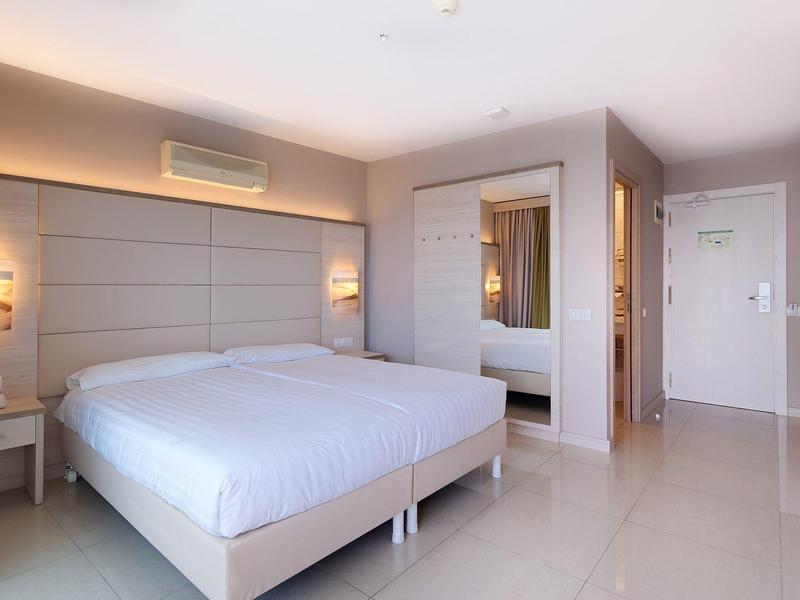 Modernes helles Schlafzimmer mit großem Bett, Nachttischen, Klimaanlage und Spiegel an der Wand.