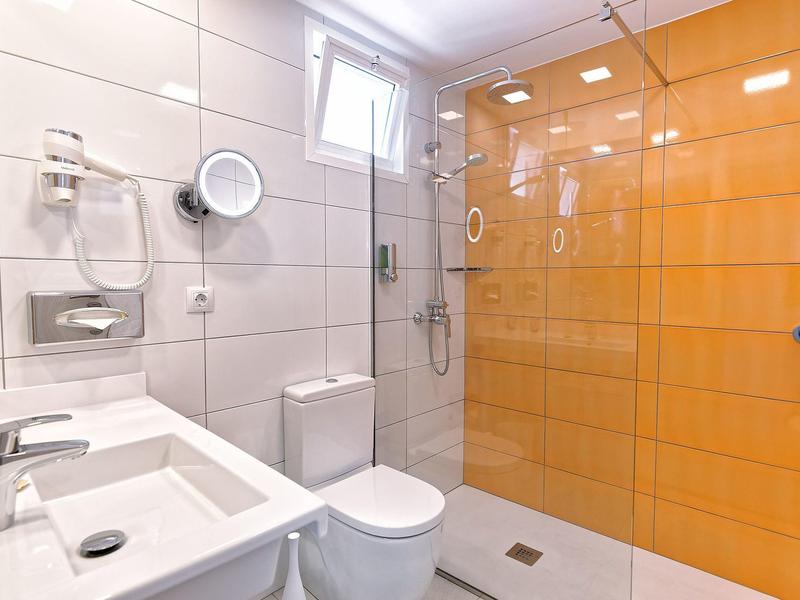 Klares Badezimmer mit weiß gefliesten Wänden, orangefarbenem Duschbereich und modernen Sanitäranlagen.