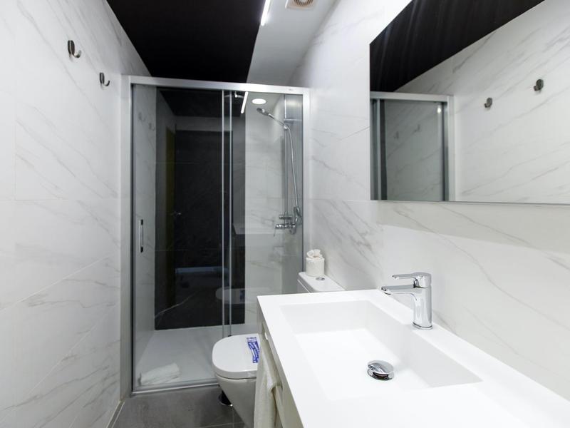 Modernes Badezimmer mit weißem Waschbecken, Glas-Duschkabine und großem Spiegel an weiß gefliesten Wänden.