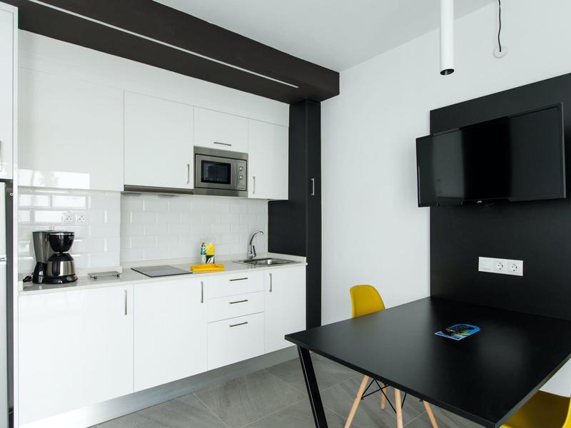 Moderne weiße Küche mit schwarzem Essbereich und gelben Stühlen in minimalistischem Raum.