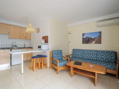 Helles Wohnzimmer mit blauer Couch, Holztisch, Küchenzeile und zwei kleinen braunen Hockern.