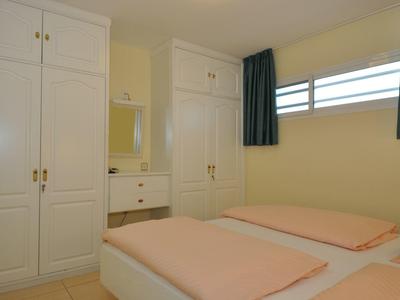 Kleines Schlafzimmer mit weißen Schränken, Doppelbett mit rosa Bettwäsche und grünen Vorhängen.