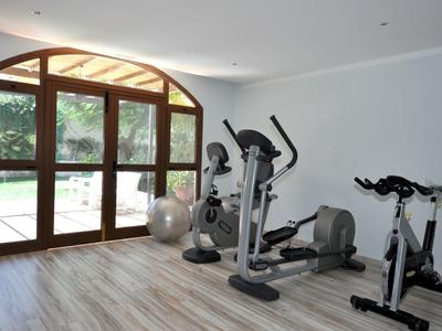 Moderner Fitnessraum mit großen Fensterbogen, Holzfußboden, Crosstrainer, Spinning-Bike und Gymnastikball.
