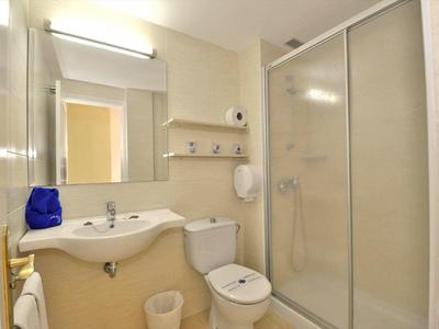 Kleines Badezimmer mit Waschbecken, Toilette, Glastür-Dusche und Spiegel mit Lichtleiste.