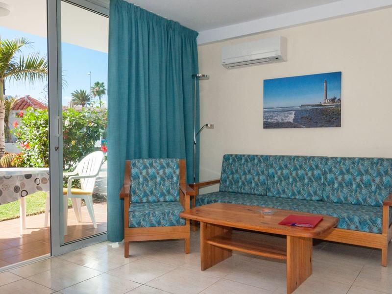 Gezellig hotelkamerhoekje met blauwe bank, fauteuil, houten tafel en uitzicht op terras.