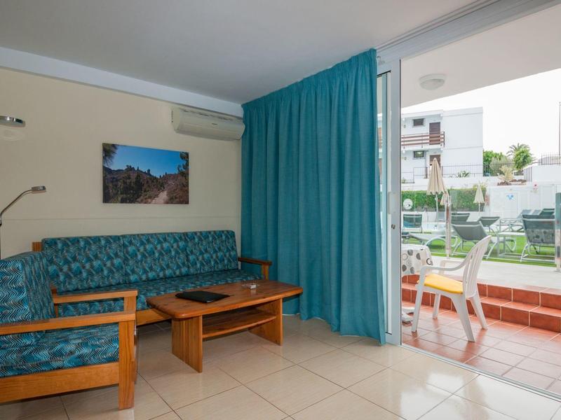 Gezellige woonkamer met blauwe bank, houten tafel en uitzicht op terras met stoelen.