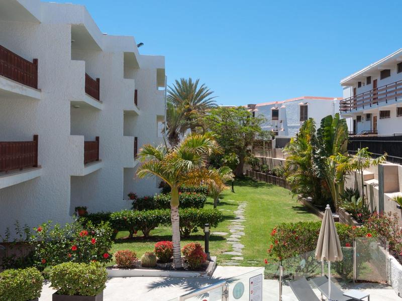 Een goed onderhouden tuin tussen witte hotelgebouwen met balkons en palmbomen.