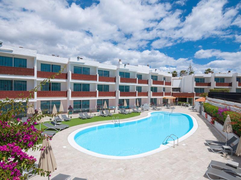 Modern hotelcomplex met U-vormig zwembad, ligstoelen en blauwe lucht