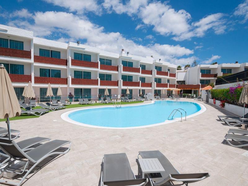 Modern hotelzwembad met ligstoelen onder een blauwe hemel met enkele wolken.