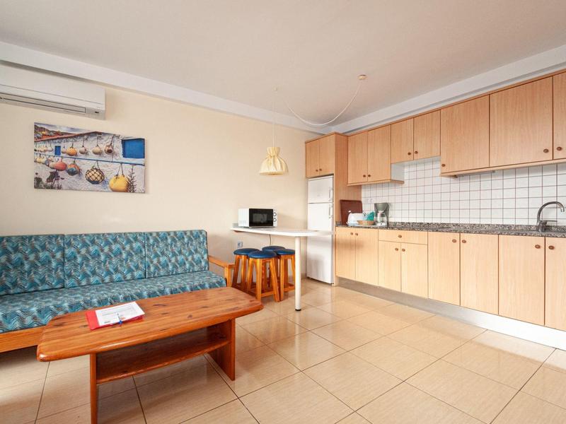 Lichte keuken met houten kasten, blauwe bank, houten tafel en witte tegels.