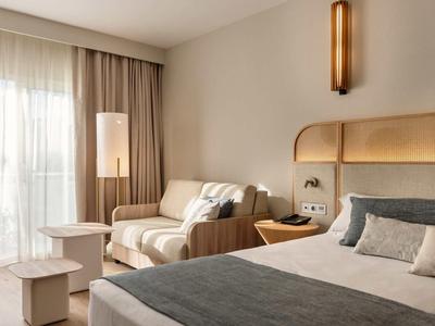 Moderní hotelový pokoj s velkou postelí, útulným posezením a měkkými závěsy u okna.