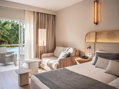 Moderní hotelový pokoj s manželskou postelí, pohovkou, stolem a balkonem s výhledem na palmy.