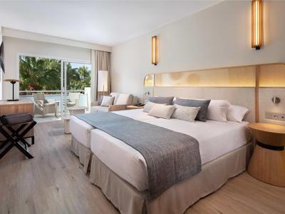 Moderní hotelový pokoj s velkou postelí, posezením a balkonem s výhledem na zeleň.