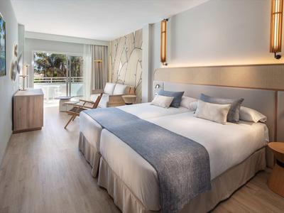 Moderní hotelový pokoj s manželskou postelí, posezením a balkonem s výhledem ven.