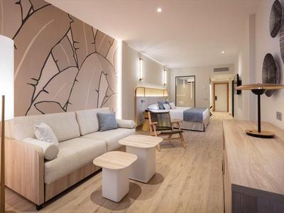 Moderně zařízený hotelový pokoj s pohovkou, křesly a dekorativním nástěnným vzorem.