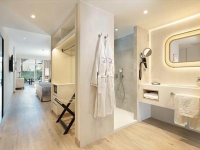 Světlá koupelna s moderním vybavením a otevřeným přístupem do ložnicové části v hotelovém pokoji.