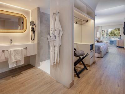 Moderní hotelový pokoj s dřevěnou podlahou, koupelnou a balkonem s stolem a židlemi.